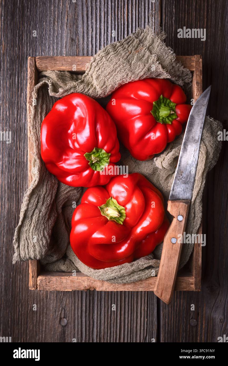 Peperoni rossi in cassetta di legno con coltello da cucina. Verdure biologiche fresche, concetto di cucina rustica Foto Stock