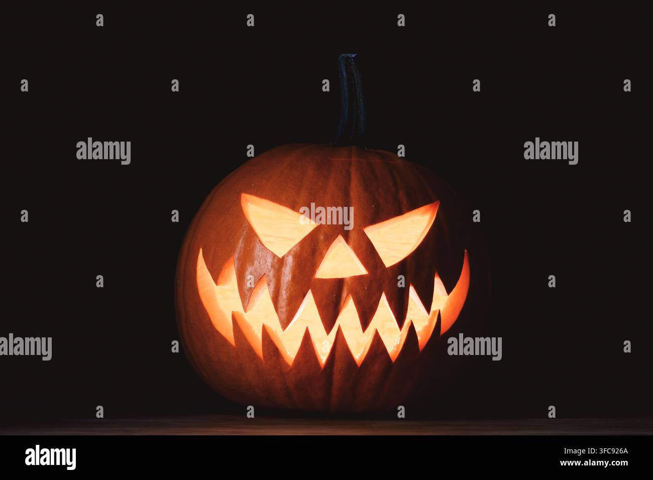 Jack-o'-lanterna illuminato con sorriso sinistro e occhi brillanti isolato su sfondo nero. Decorazione festiva di Halloween che crea un'atmosfera autunnale spettrale Foto Stock