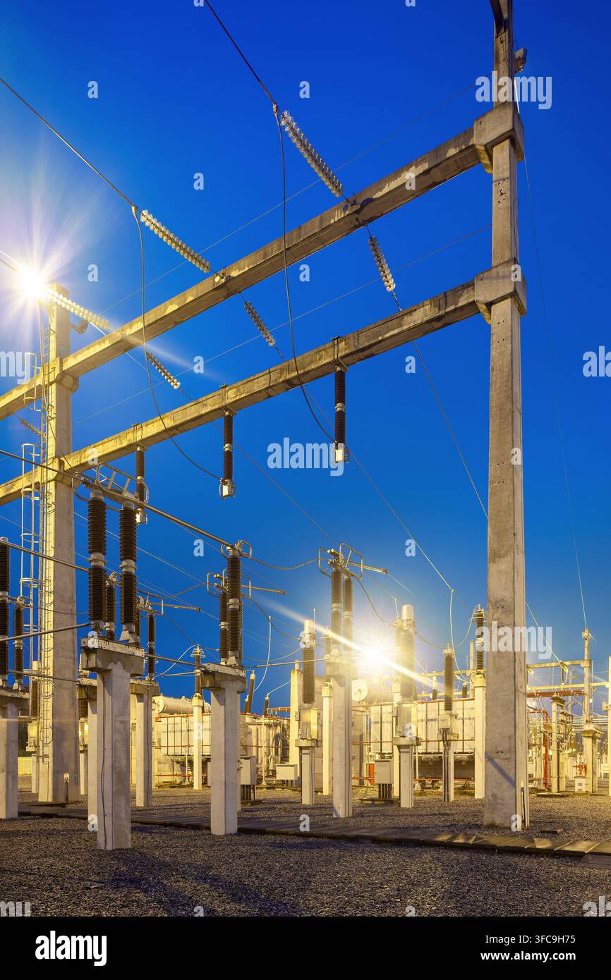 Una sottostazione elettrica illuminata con apparecchiature ad alta tensione, trasformatori e strutture di supporto in cemento al crepuscolo in Brasile. Foto Stock