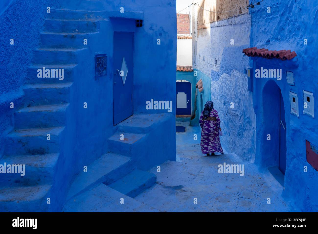 Una donna irriconoscibile in abito tradizionale che cammina in un vicolo dipinto di blu a Chefchaouen, in Marocco. Foto Stock