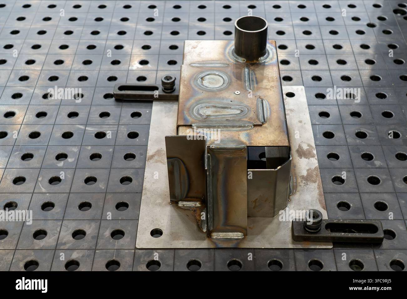 Componente in acciaio saldato fissato su un tavolo di saldatura 3D modulare con fori di fissaggio a griglia in un laboratorio di fabbricazione metallica industriale Foto Stock