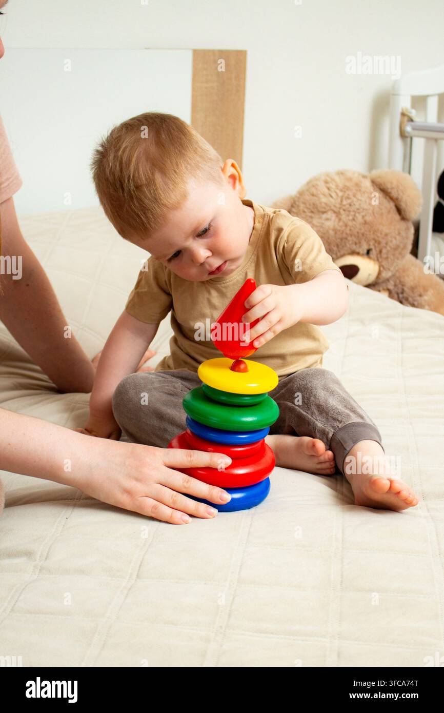 Bambino di due anni concentrato nello stacking degli anelli giocando con un giocattolo a piramide di plastica. Crescita delle capacità logiche e di pensiero. I colori vivaci attirano l'attenzione. Motricità fine Foto Stock