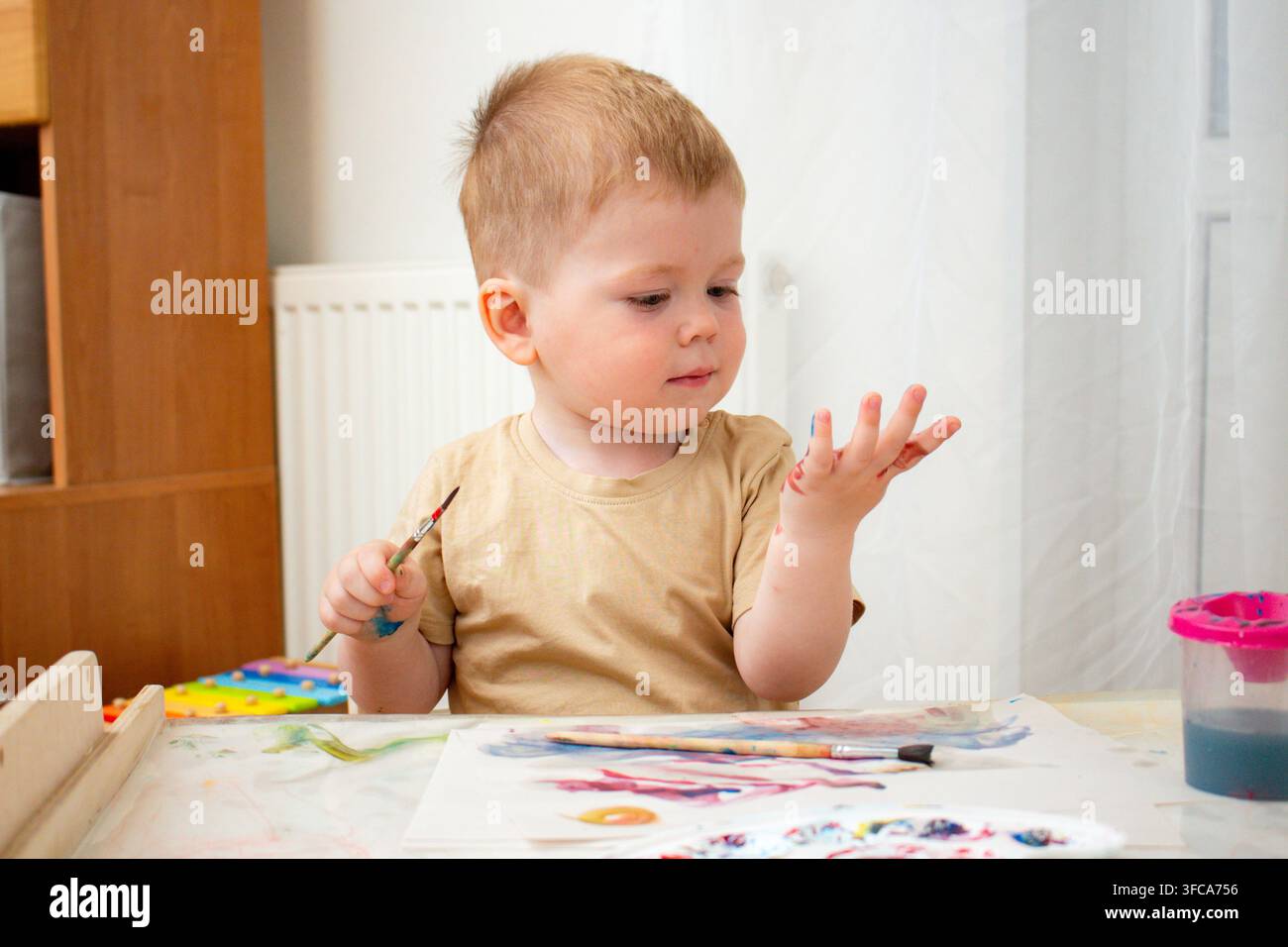 Bambino che mescola acquerelli con le dita sulla carta. Apprendimento tattile sulla miscelazione dei colori. Il gioco sensoriale rafforza le connessioni neurali. Terapia artistica e ar Foto Stock