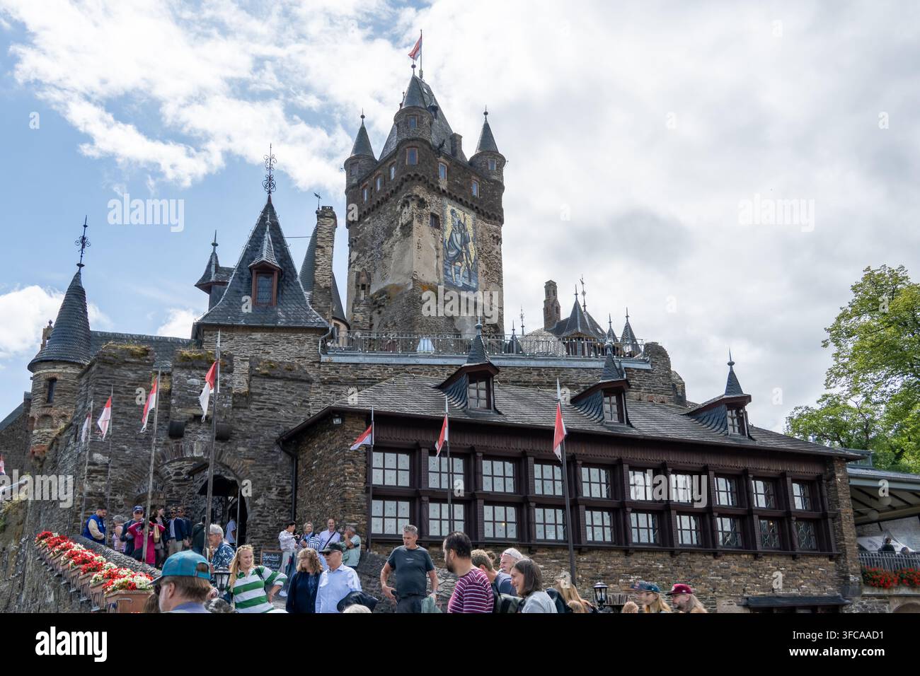 Cochem Germania - 2 ago 25: Castello di Reichsburg Cochem con visitatori, mura di pietra, torri, bandiere e un cielo nuvoloso a Cochem, Germania. Foto Stock