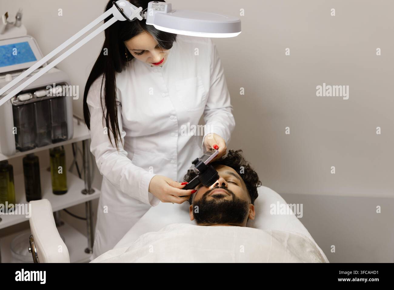 Dottoressa che utilizza un dermatoscopio per esaminare la pelle del viso di un paziente maschio a scopo dermatologico e di cura della pelle in una clinica Foto Stock
