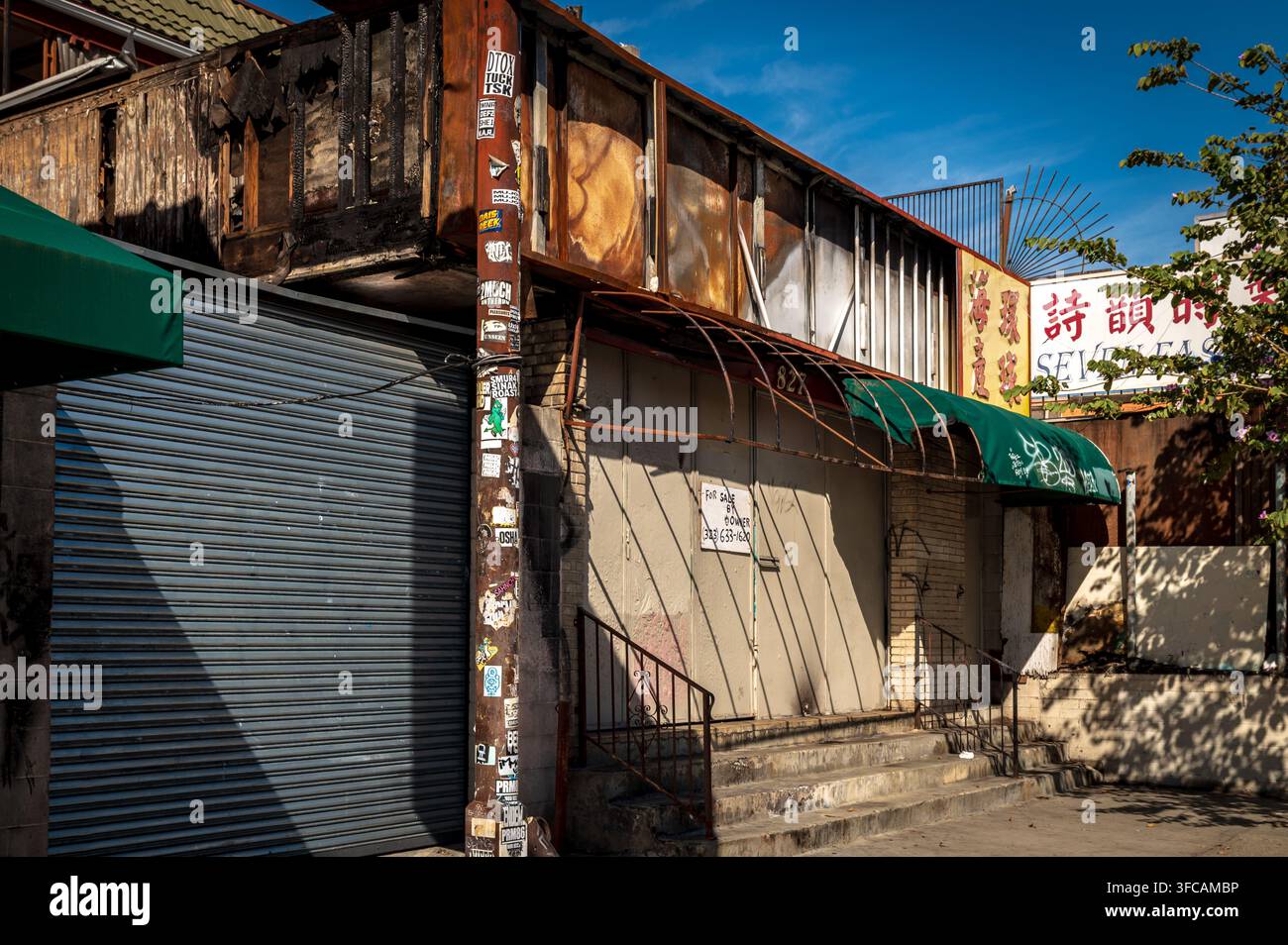 LOS ANGELES, CALIFORNIA — 12 febbraio 2026: Un edificio commerciale danneggiato da un incendio con serrande metalliche, un cartello "Vendita diretta da proprietario", tende da sole, bastone per le utenze Foto Stock
