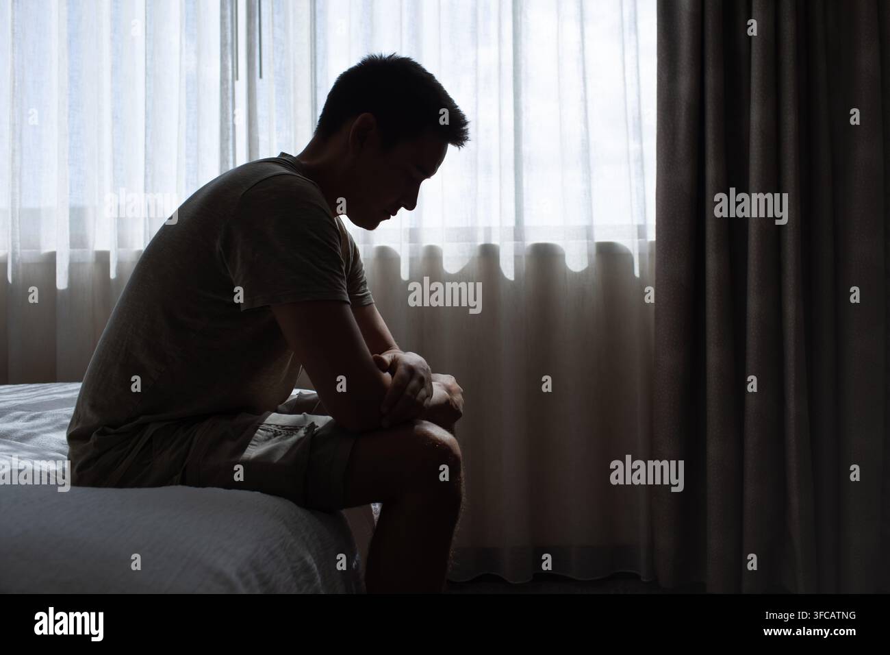 Uomo solo seduto su un letto che si sente triste. Foto Stock