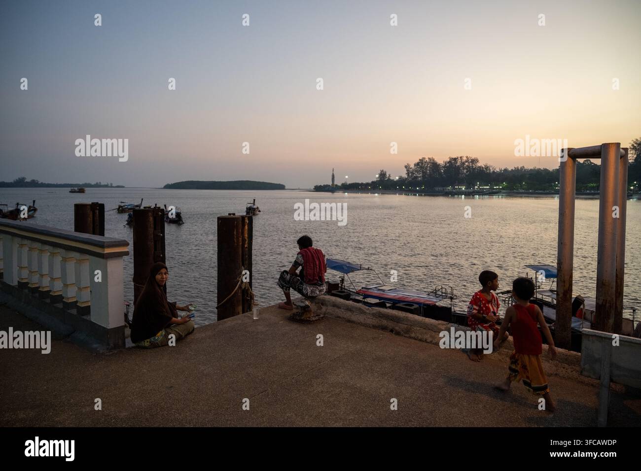 KRABI, THAILANDIA — 5 MARZO 2026: Adulti e bambini attendono accanto alle barche a lunga coda presso l'attracco dei traghetti di Koh Klang al crepuscolo. Foto Stock