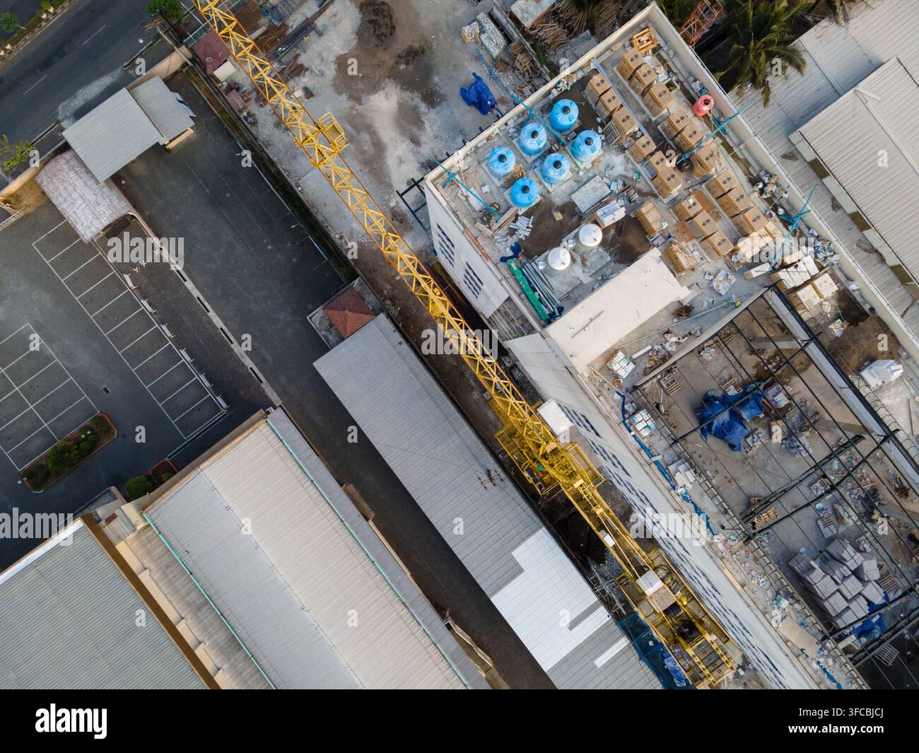Vista aerea di un cantiere edile con una gru torre gialla, un edificio con serbatoi d'acqua sul tetto e parcheggi adiacenti a Purwokerto Foto Stock