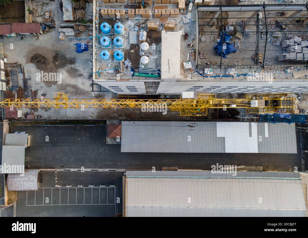 Vista aerea di un cantiere edile con una gru torre gialla, un edificio industriale con serbatoi d'acqua blu sul tetto e strutture con tetto in metallo Foto Stock