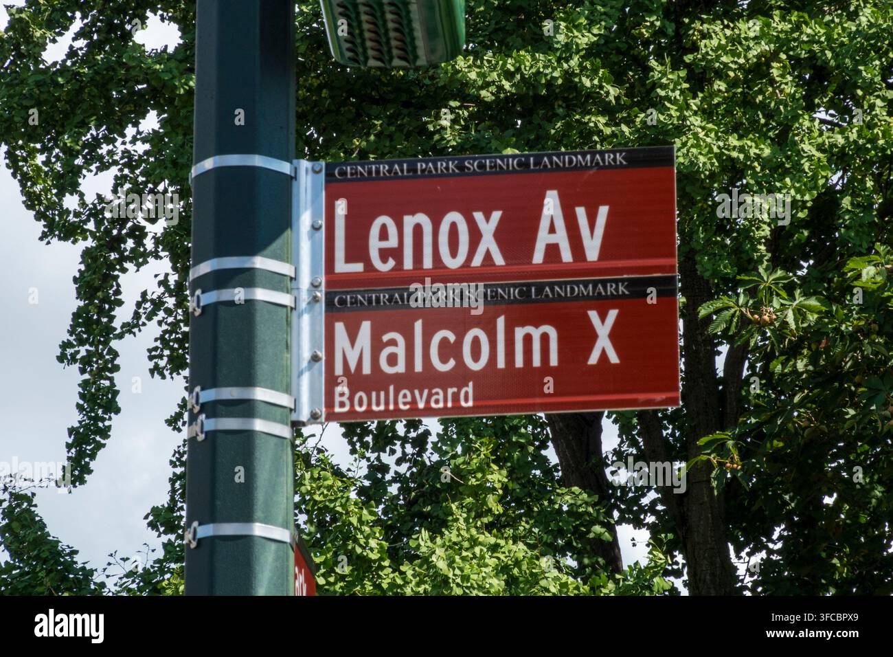 New York, NY – USA – 23 ago 2026 Segno stradale rosso al Landmark Scenic di Central Park mostra "Lenox Av" nella sezione superiore e "Malcolm X Boulevard" su t Foto Stock