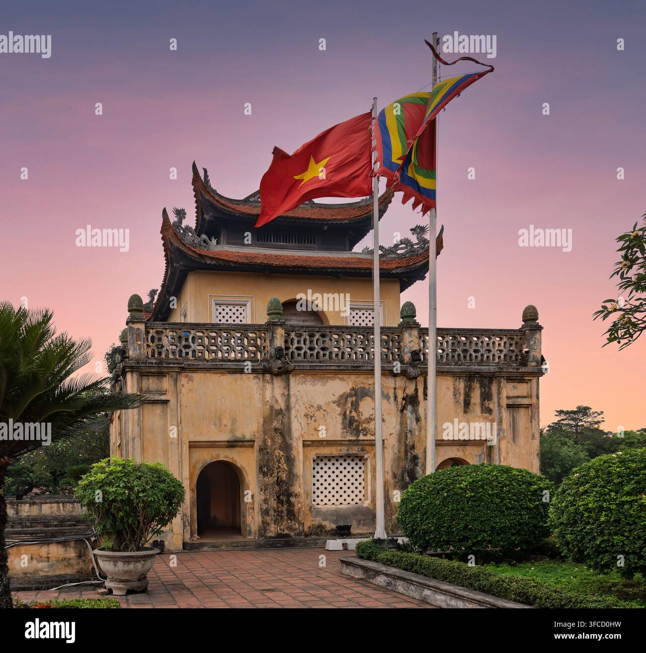 La porta storica Doan Mon alla Cittadella imperiale di Thang Long a Hanoi, Vietnam, con la bandiera nazionale e una bandiera buddista tradizionale che sventola di nuovo Foto Stock