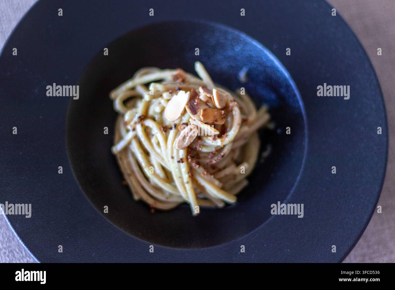 Vista ad angolazione alta con effetto sfocato di spaghetti di grano integrale con salsa cremosa, scaglie di mandorle e pangrattato in una ciotola di ceramica scura Foto Stock