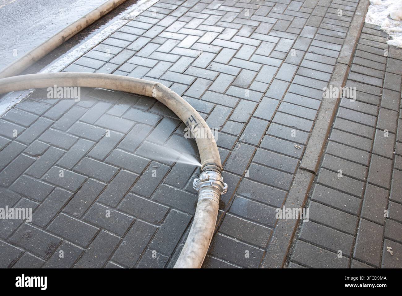 Mano da pompiere scaduta, perdita d'acqua. L'acqua fuoriesce da un buco in un tubo industriale. Il tubo antincendio giace sulla strada Foto Stock