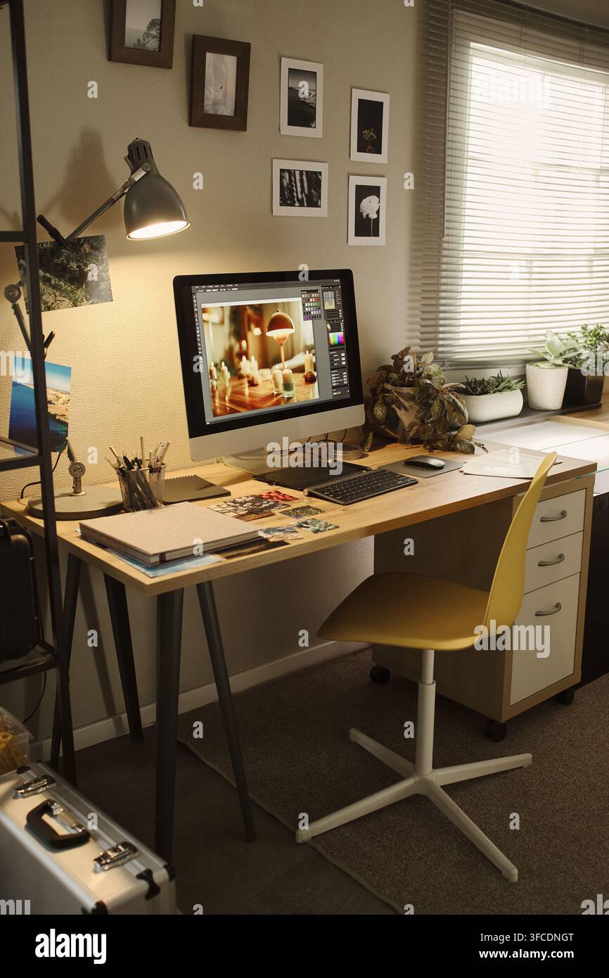 Immagine verticale di uno spazio di lavoro creativo in ufficio domestico con monitor del computer che mostra un software di editing fotografico. La scena rappresenta il lavoro remoto e il marketing di carriera nella progettazione digitale Foto Stock
