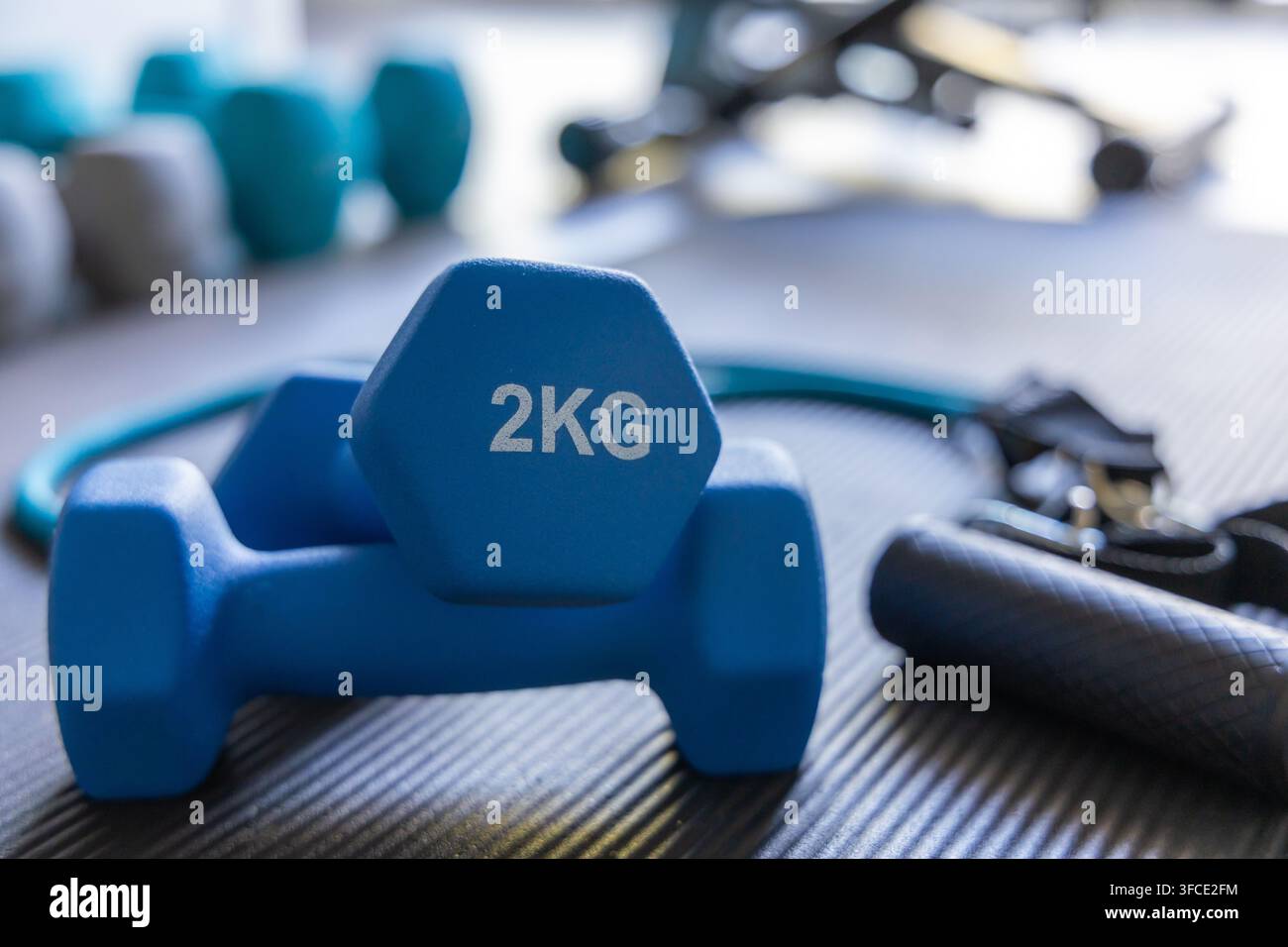 Vista ravvicinata di manubri blu da 2 kg e di una banda di resistenza disposti su un tappetino da palestra ruvido, pronti per una sessione di allenamento Foto Stock