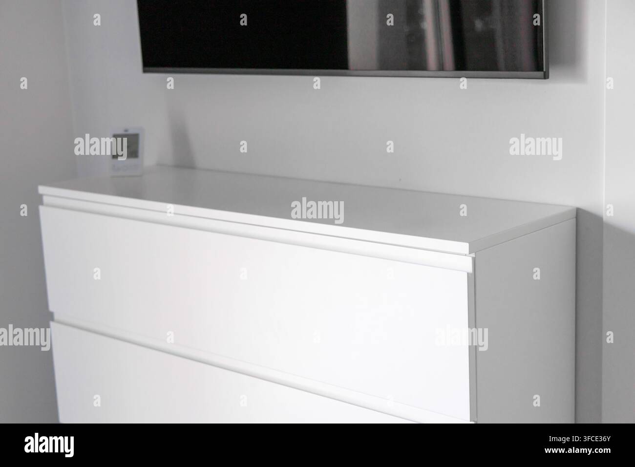 Una configurazione di camera da letto pulita e contemporanea con un comò bianco elegante e una TV a schermo piatto montata su una parete neutra Foto Stock