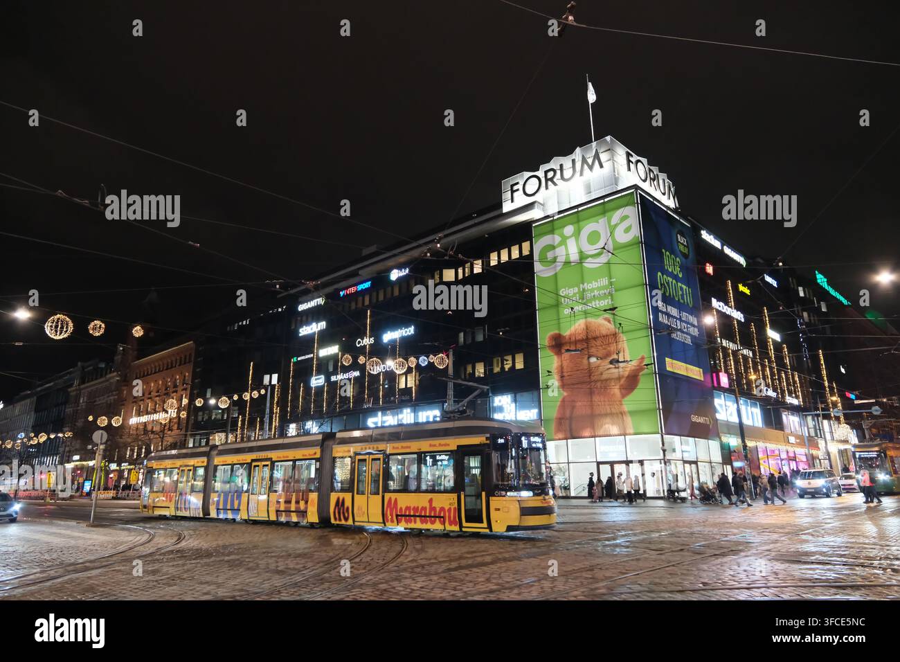 Helsinki, Finlandia-30 nov. 2025: vista notturna del tram che passa davanti al centro commerciale Forum di Helsinki Foto Stock