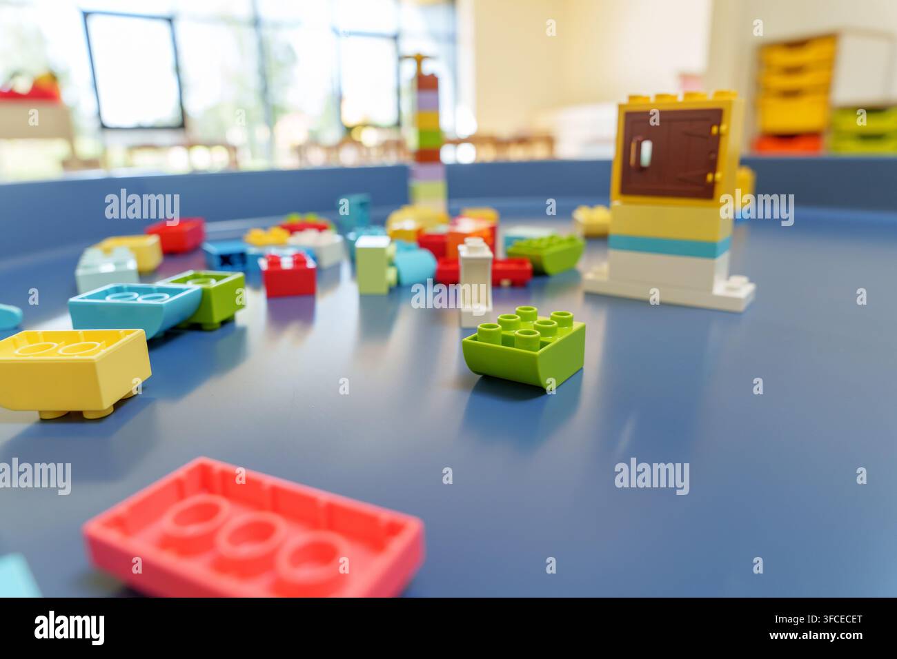 Blocchi da costruzione in plastica colorati sparsi su un tavolo da gioco blu in un'aula luminosa, concetto di educazione prescolare e gioco creativo. Foto Stock