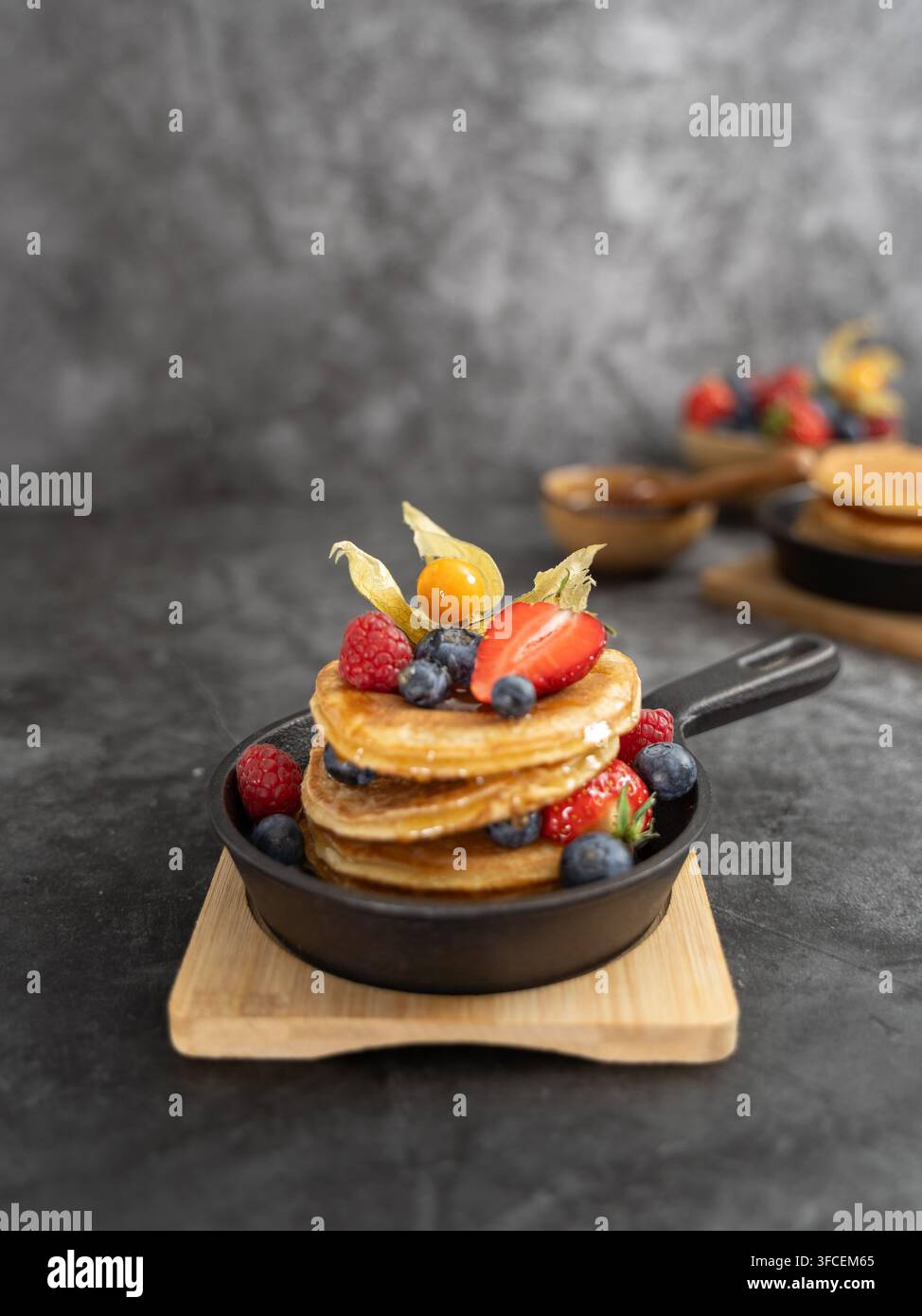 Pancake fatti in casa guarniti con frutti di bosco freschi e frutta, serviti su una tavola di legno con glassa al miele e stile alimentare scuro rustico Foto Stock