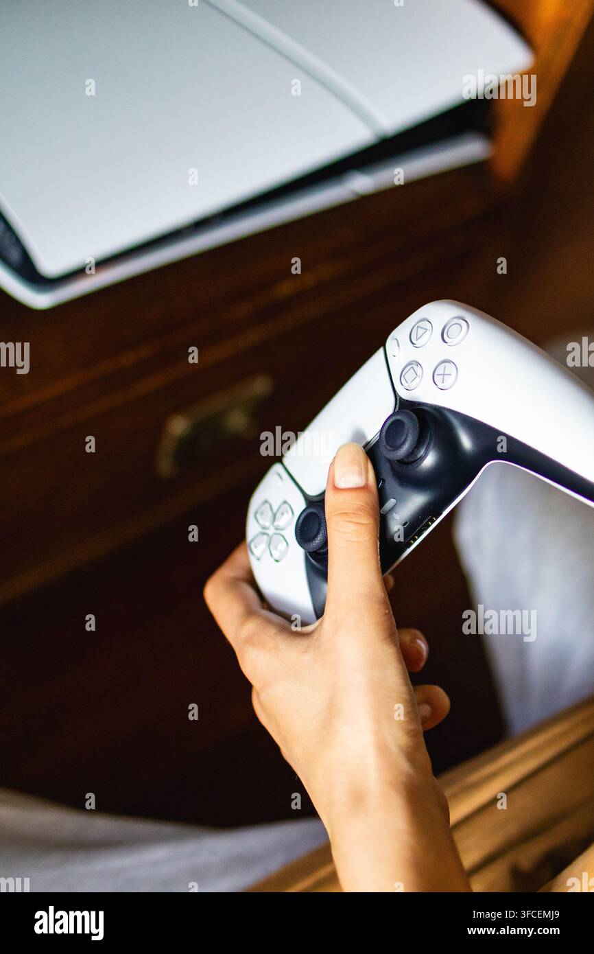 Mano che tiene un controller bianco per videogiochi vicino alla console durante l'installazione per una sessione di gioco in primo piano. Concetto di preparazione al gioco e interazione con le mani Foto Stock