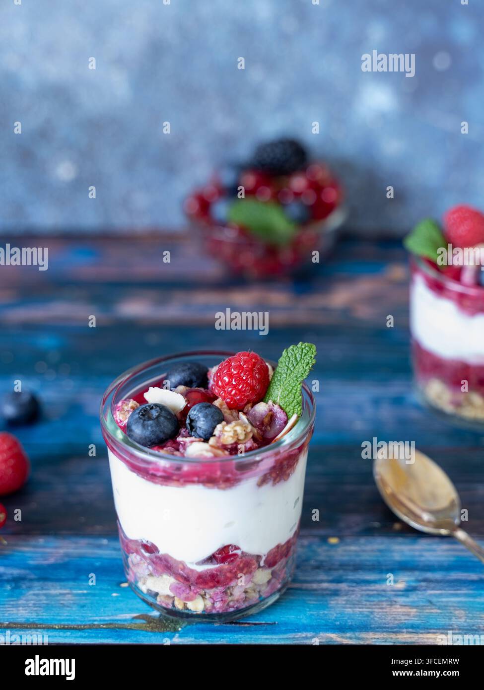 Prima colazione di un dessert mascarpone a strati individuale ricoperto di frutti freschi e menta, con granola croccante visibile tra lo strato cremoso e quello fruttato Foto Stock