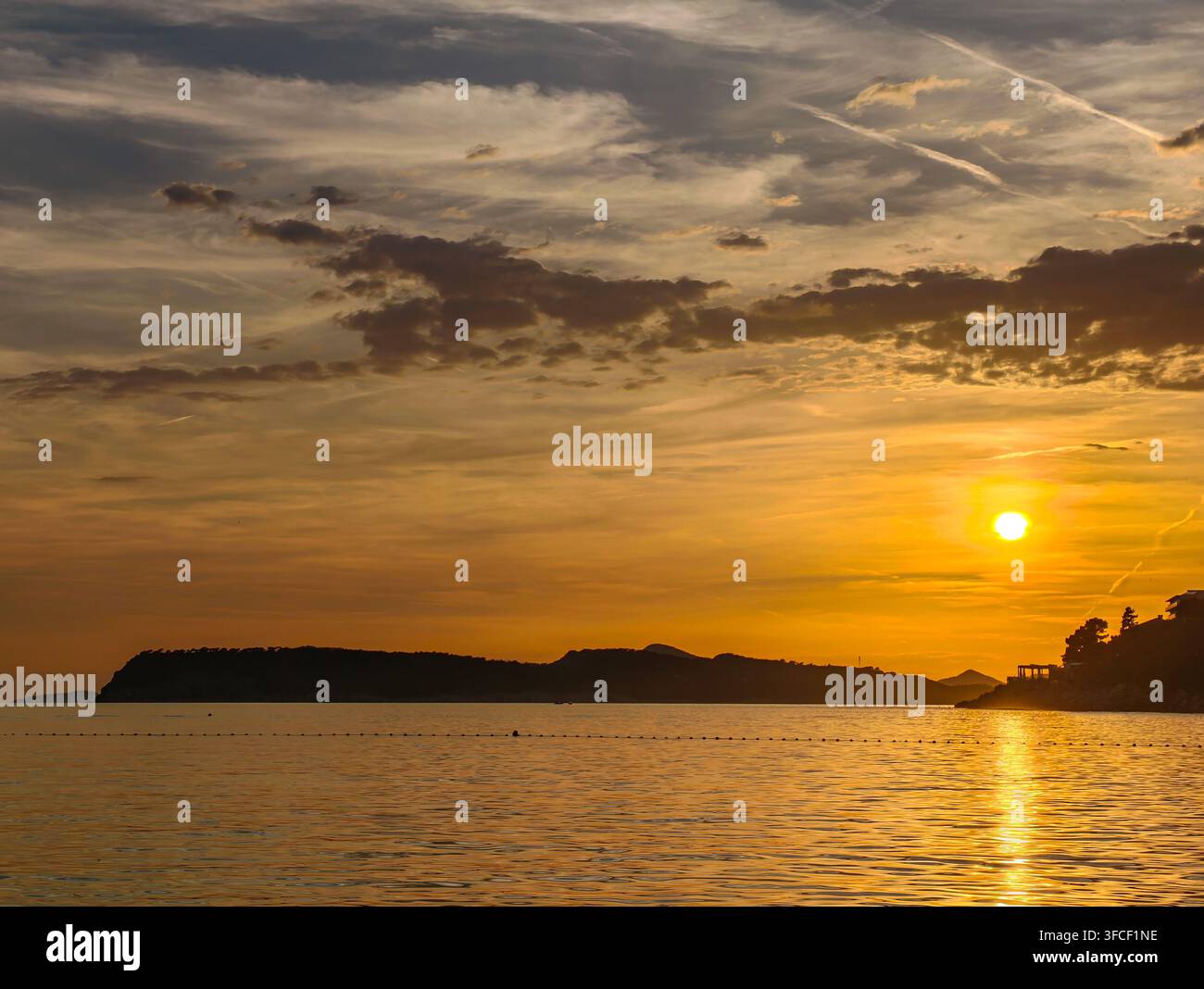 Un tramonto dorato mozzafiato dipinge il cielo sopra le acque calme dell'oceano, proiettando silhouette sulla costa frastagliata in un momento di pura pace. - Immagine stock catturata con smartphone