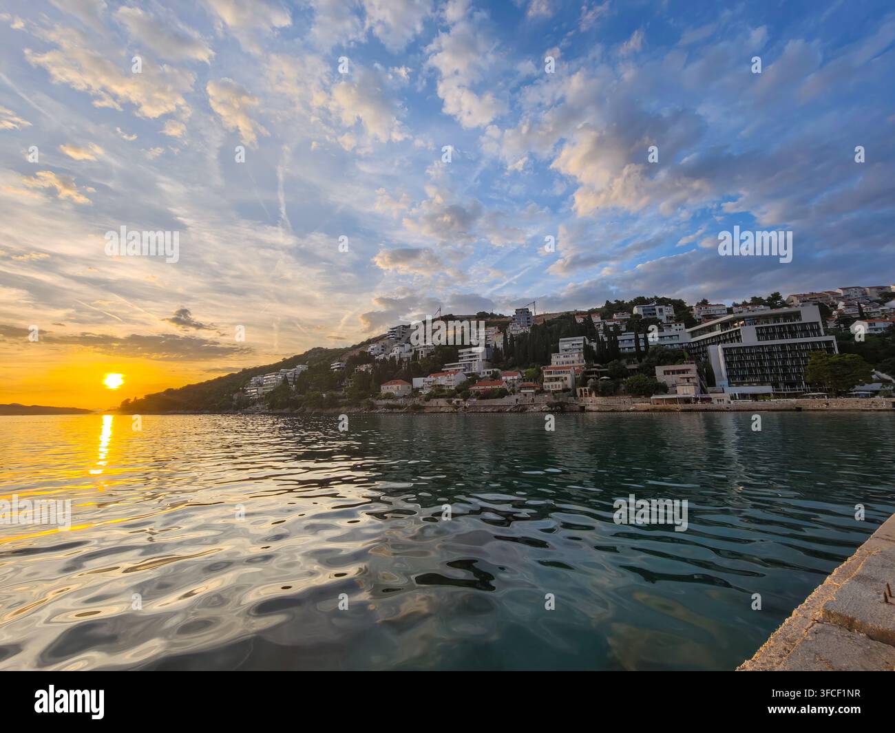 Una scena tranquilla dell'ora dorata che si affaccia su una riva di ciottoli con cieli nuvolosi drammatici sopra un tranquillo paesaggio costiero mediterraneo di Lapad. - Immagine stock catturata con smartphone