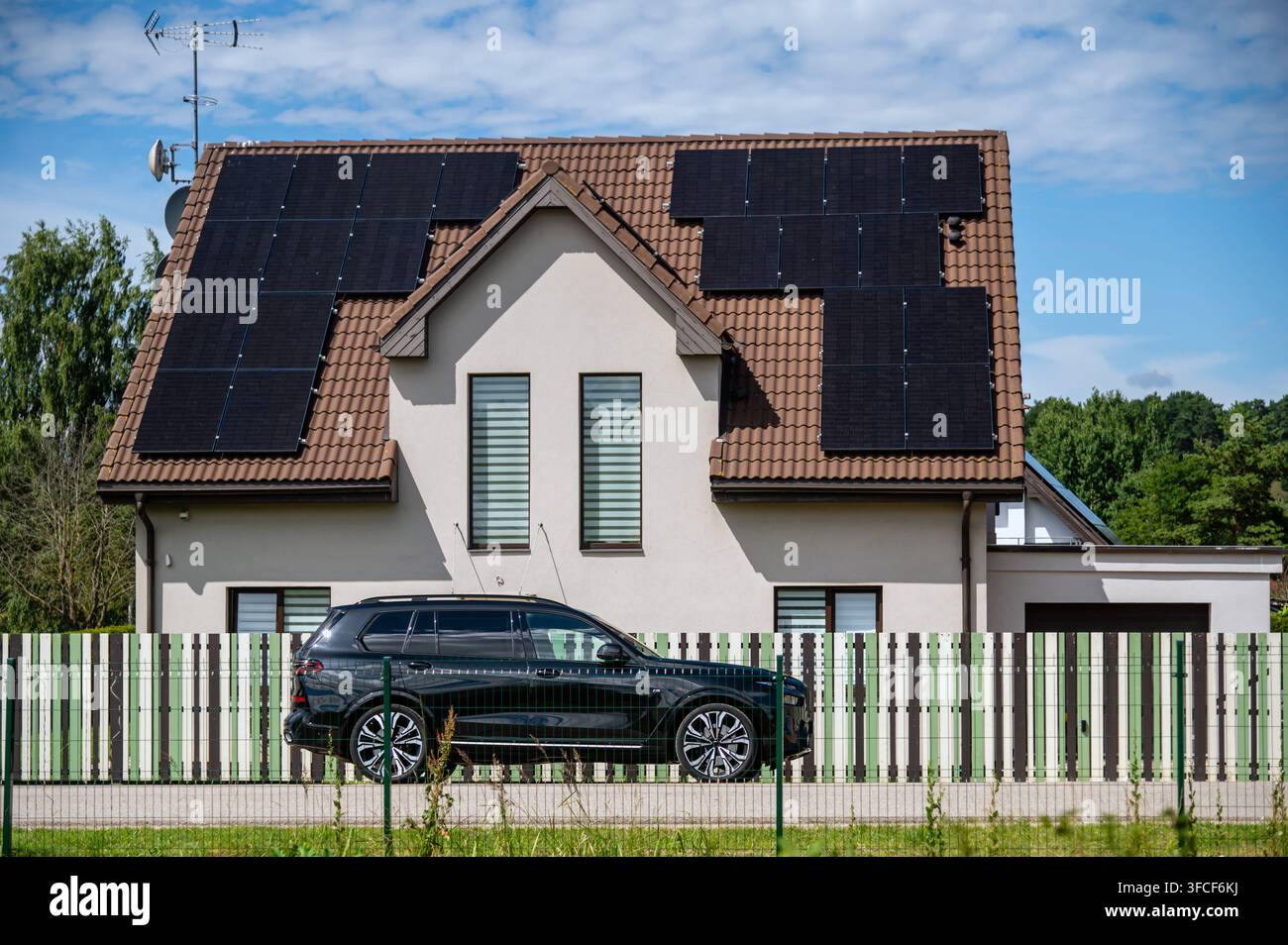 Tukums, Lettonia – 10 luglio 2026: Pannelli solari sono posizionati sul tetto di una casa con un'auto nera parcheggiata a Tukums, Lettonia Foto Stock