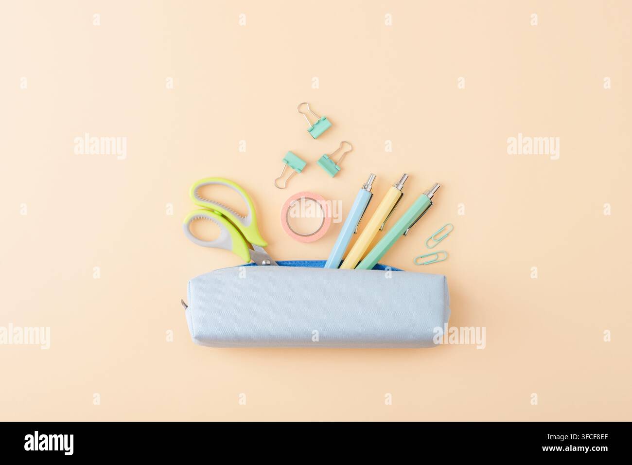 Materiali di cancelleria pastello disposti attorno a una trousse blu su uno sfondo pesca, con ampio spazio per scuola, ufficio, studio e creatività Foto Stock