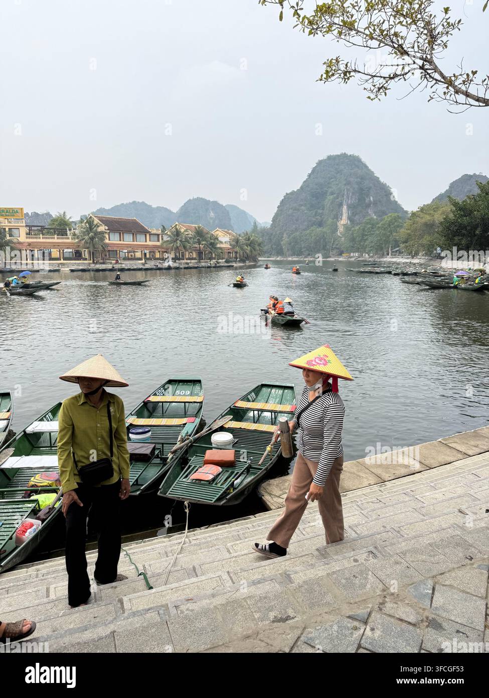 Guide di remo in abiti conici in attesa che i turisti saliscano sui loro sampan a Tam Coc nella provincia di Ninh Binh nella regione del delta del Fiume Rosso nel nord del Vietnam - Immagine stock catturata con smartphone