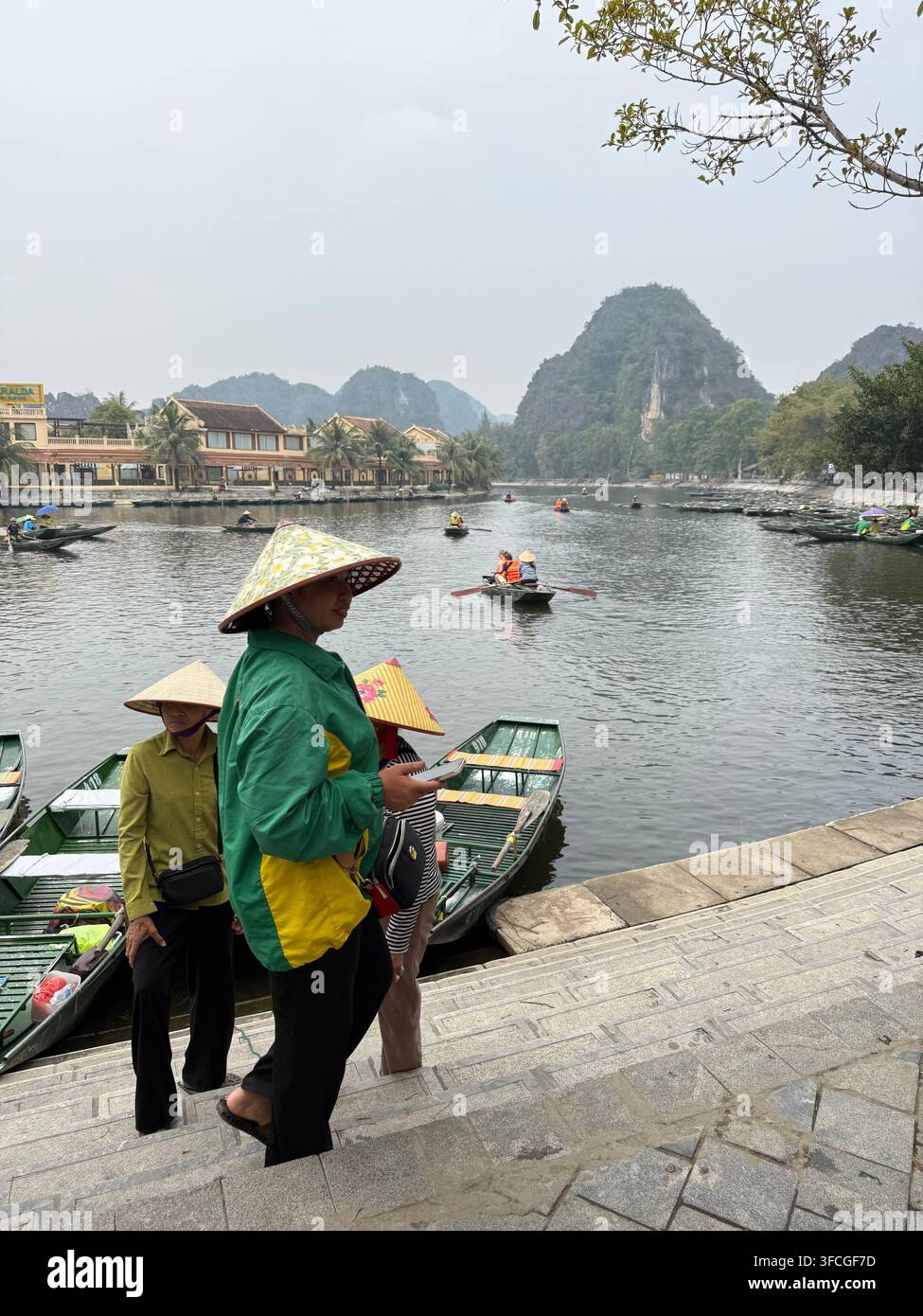 Guide di remo in abiti conici in attesa che i turisti saliscano sui loro sampan a Tam Coc nella provincia di Ninh Binh nella regione del delta del Fiume Rosso nel nord del Vietnam - Immagine stock catturata con smartphone
