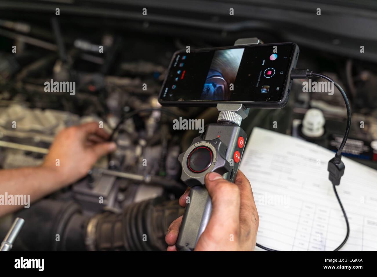 Smartphone montato supporta l'ispezione del telefono nel vano motore mentre le mani stabilizzano il controller e il cavo alimenta energia o dati. Lo schermo è rivolto verso l'utente per una precisione Foto Stock
