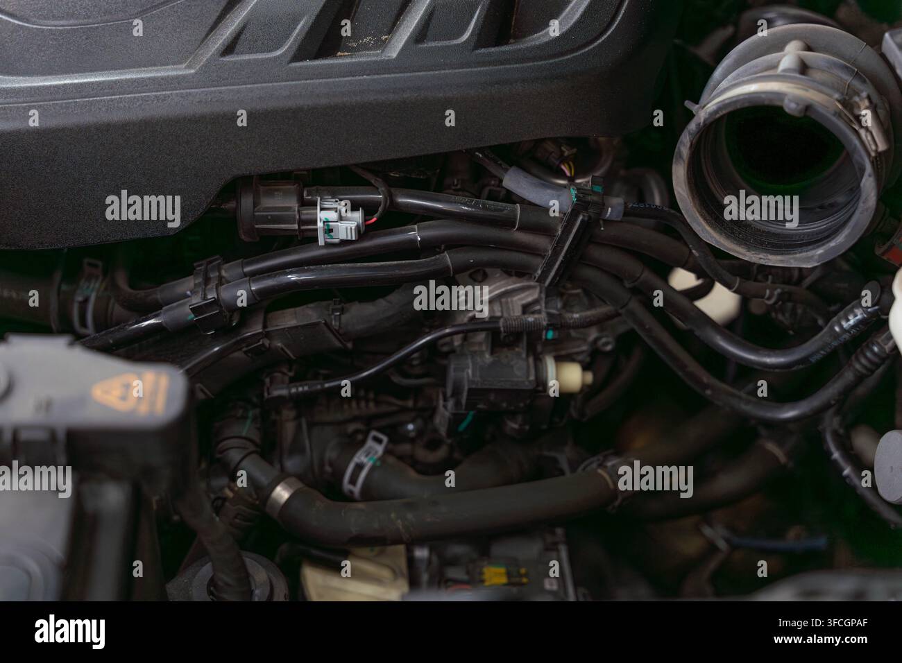 Il vano motore dell'auto mostra tubi a strati, prese elettriche, condotti di aspirazione in un vano di servizio compatto. Copriplastiche scuri e morsetti metallici definiscono Foto Stock