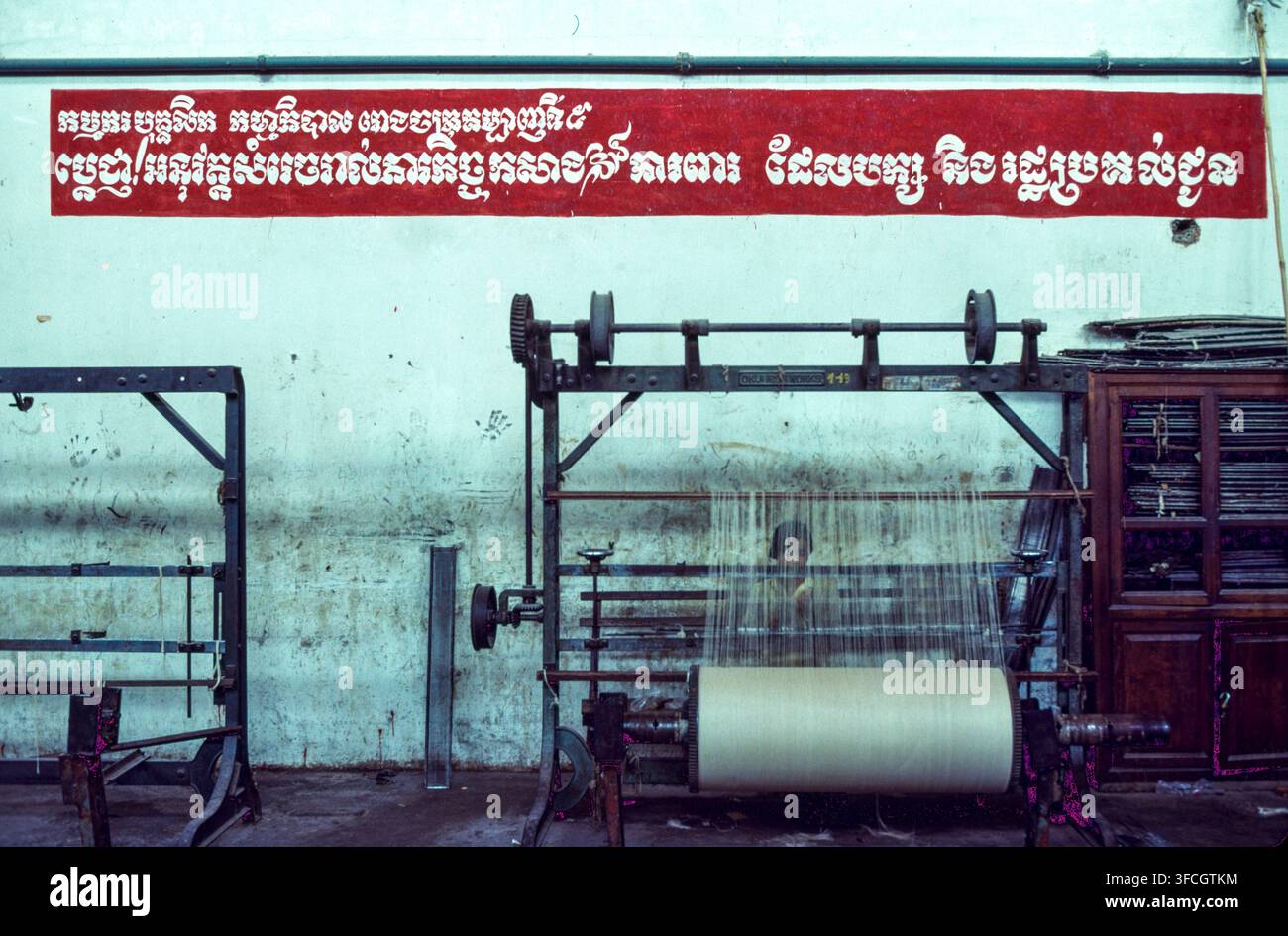 Lo slogan di questa fabbrica a Phnom Penh recita: "I lavoratori e il personale della Fabbrica di Tessitura n. 5 si impegnano a portare a termine tutti i compiti di produzione affidati loro dal Partito e dallo Stato." Foto Stock