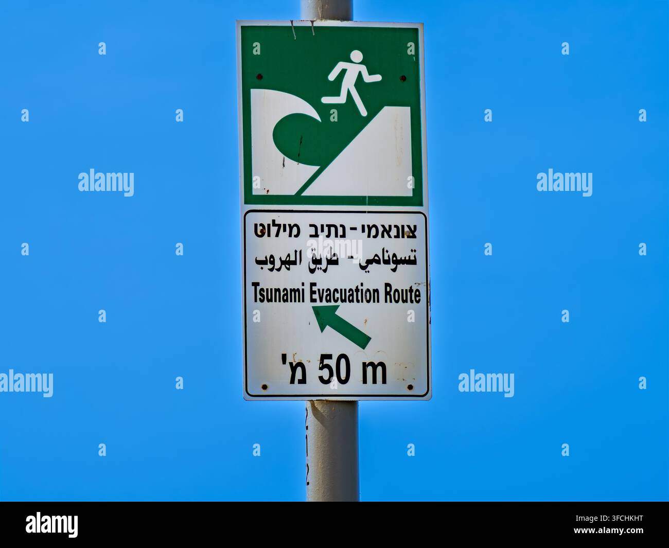 Un cartello di avvertimento per la via di evacuazione da uno tsunami su un palo contro un cielo blu limpido a Tel Aviv, Israele, che indica la direzione e la distanza verso la sicurezza a Heb Foto Stock