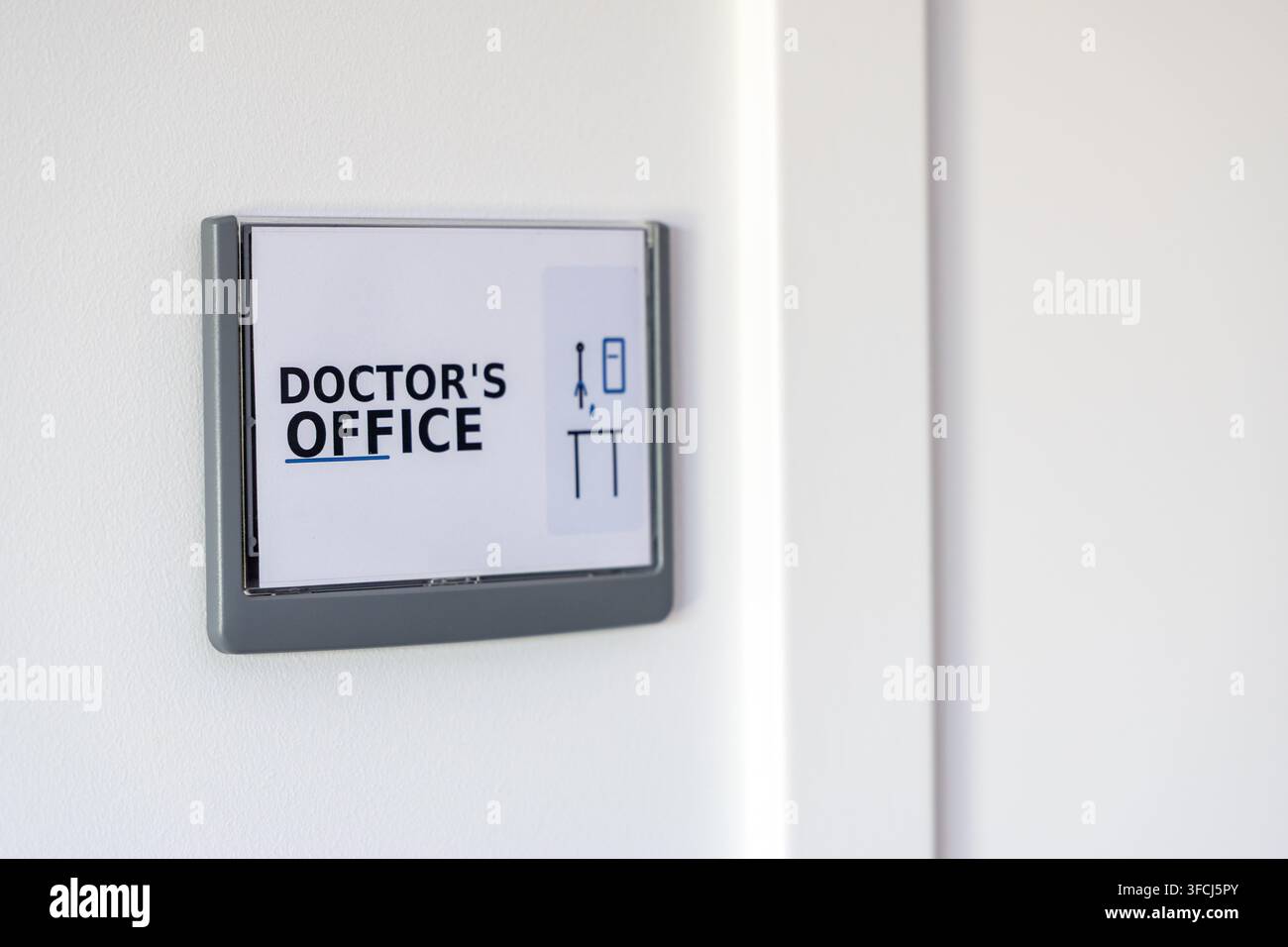 Un cartello chiaro che indica uno studio medico è montato su un muro bianco minimalista, suggerendo una struttura medica moderna Foto Stock