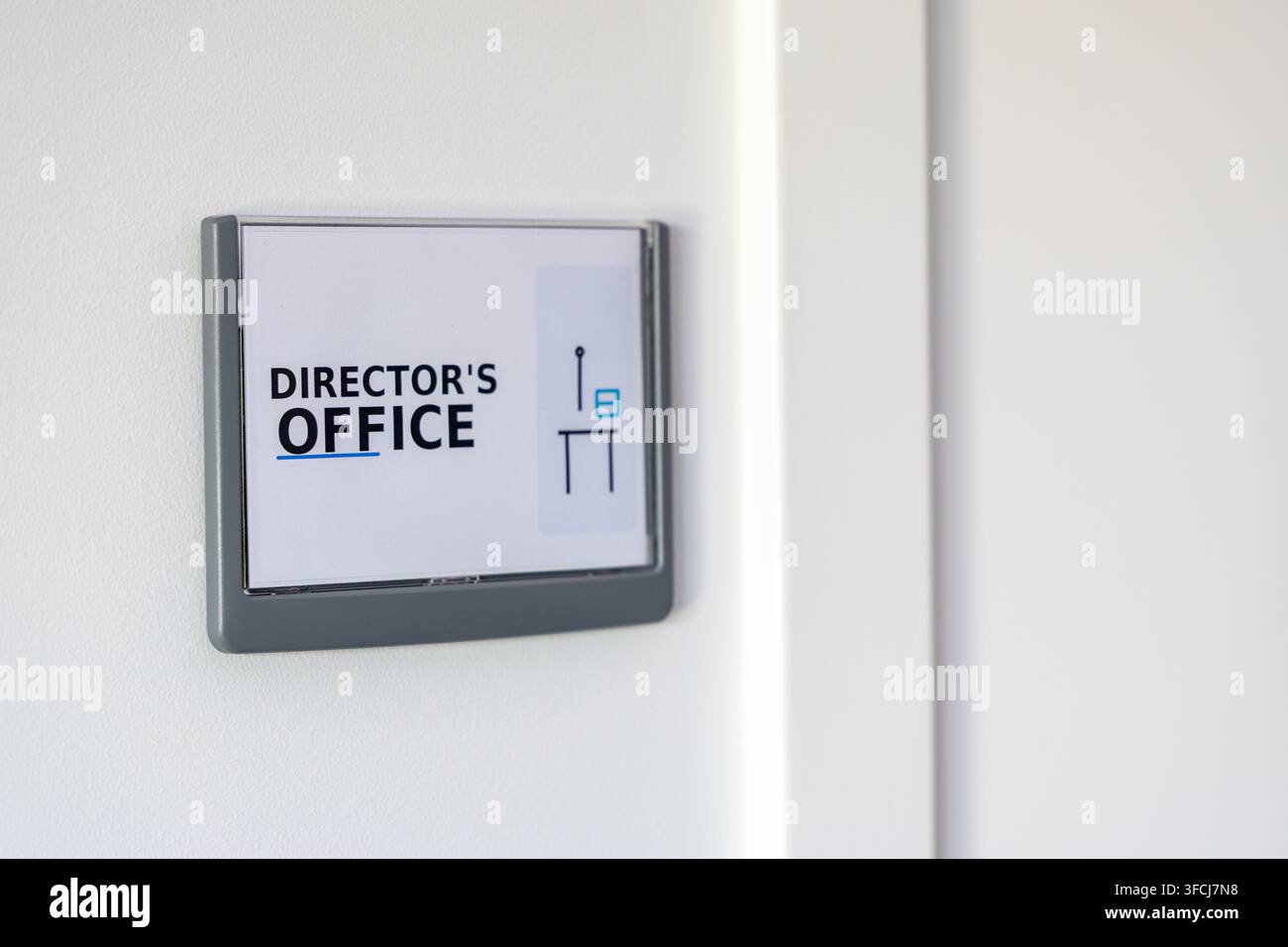 Un cartello moderno che indica l'ufficio del direttore è montato su un muro bianco minimalista, suggerendo un ambiente aziendale professionale Foto Stock