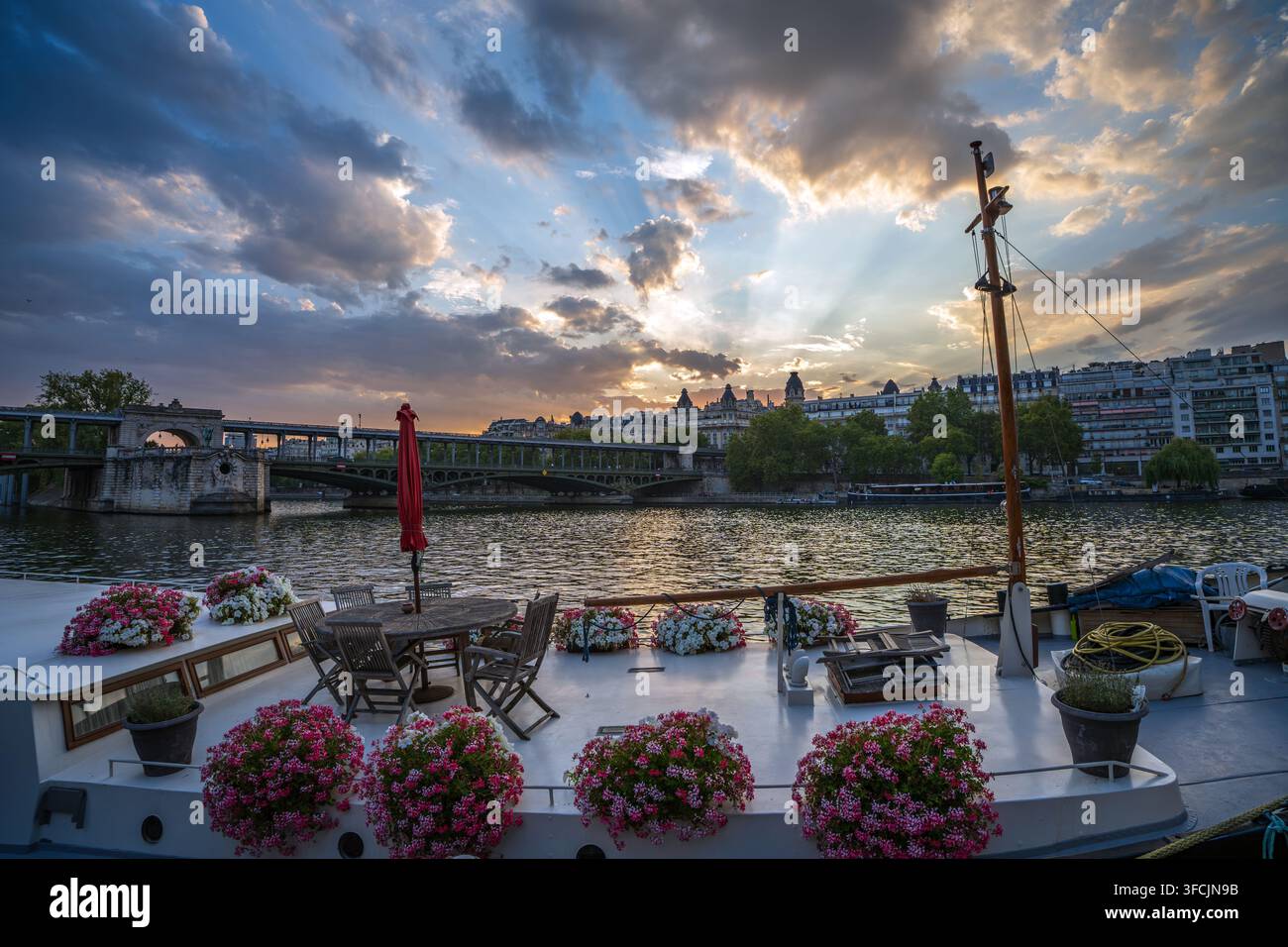 Ponte di una casa galleggiante decorata con fiori sulla Senna di fronte al Pont de Bir-Hakeim sotto un drammatico cielo al tramonto a Parigi, Francia. Foto Stock