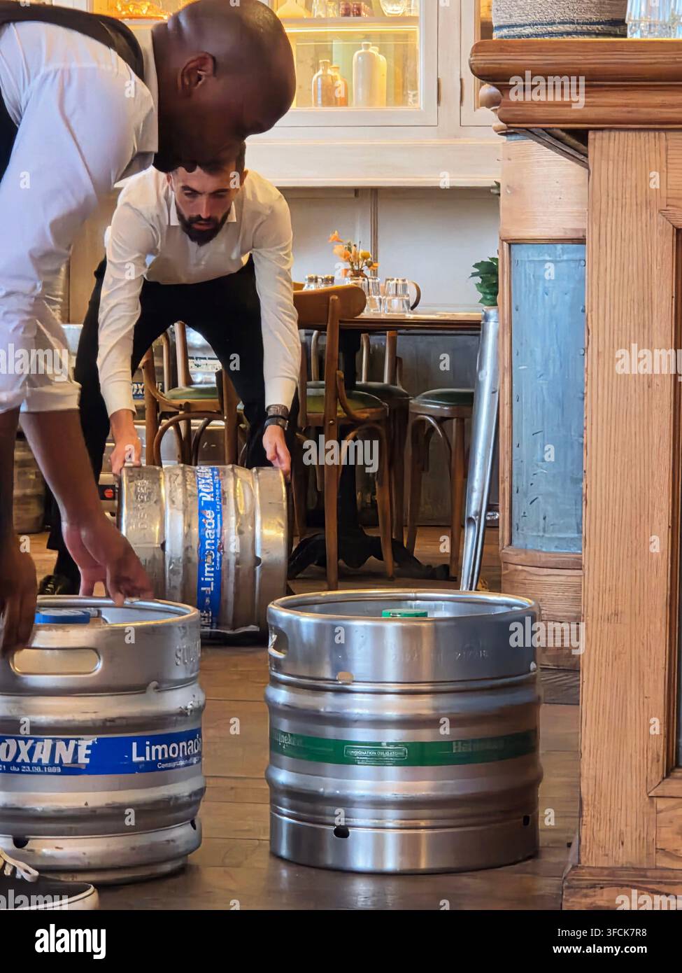 I membri del personale del ristorante spostano e sistemano pesanti fusti di bevande in acciaio inossidabile all'interno di un locale di ristorazione. Foto Stock