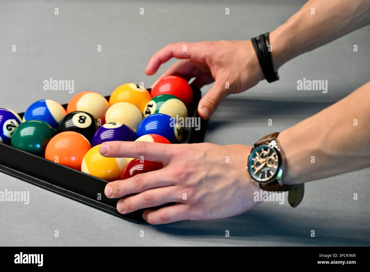 un giocatore che usa entrambe le mani per posizionare un supporto triangolare di plastica pieno di palle da biliardo numerate multicolori su un tavolo da biliardo. Foto Stock
