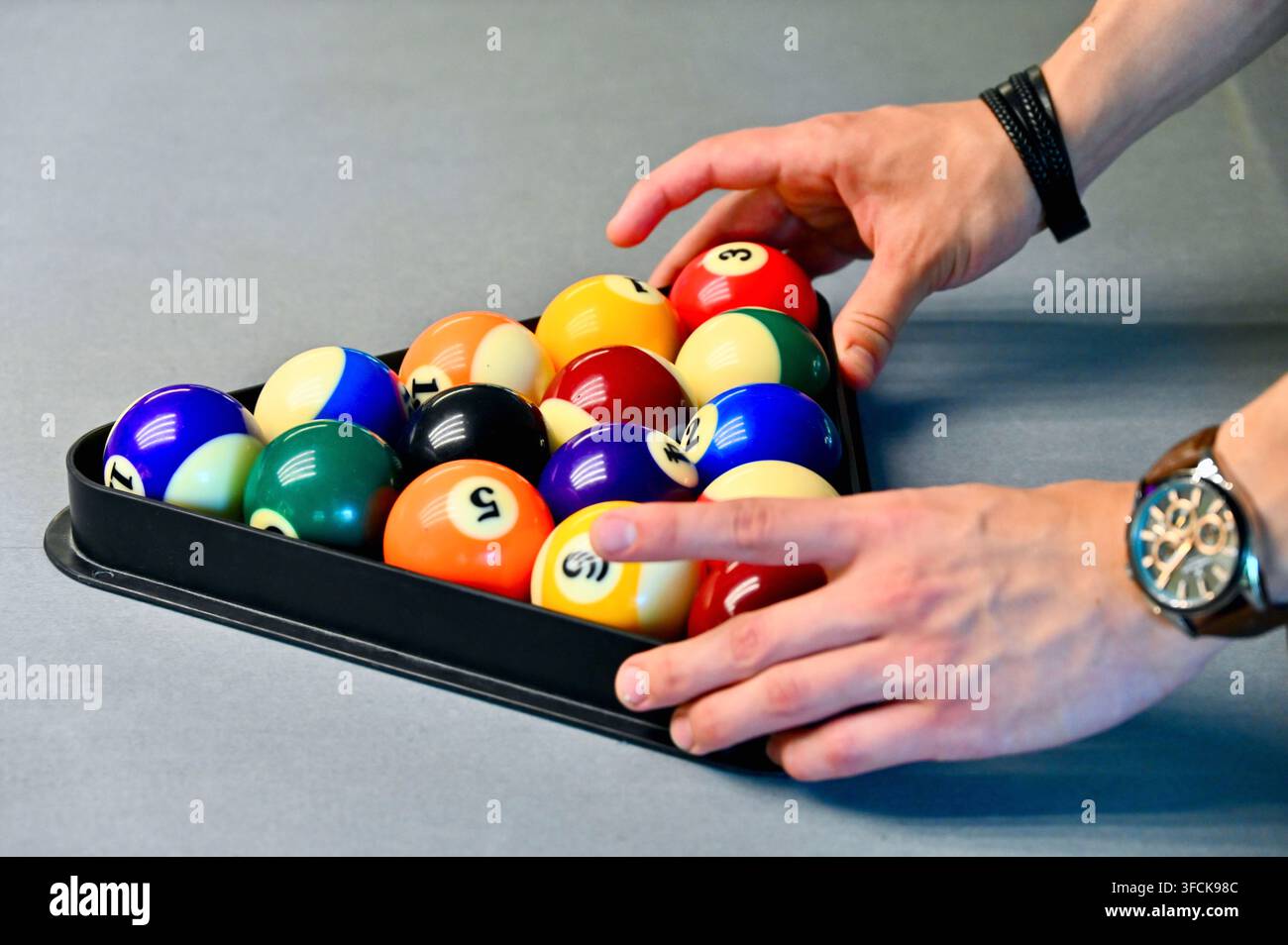 Uno scatto che mostra un giocatore che usa entrambe le mani per posizionare un rastrelliera triangolare di plastica piena di palle da biliardo numerate multicolori su un tavolo. Foto Stock