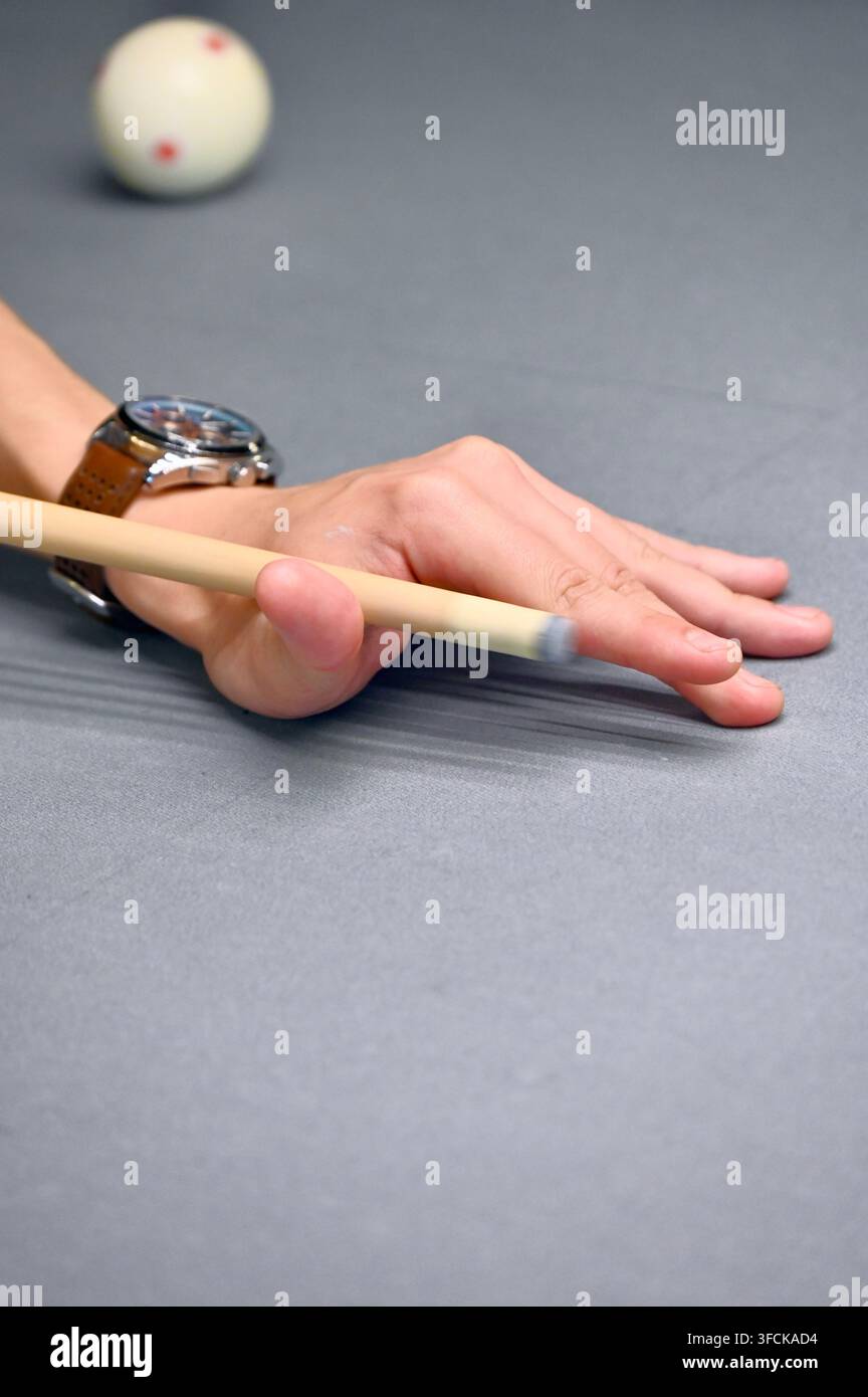 Una fotografia verticale in studio che cattura un primo piano della mano di una persona che forma un ponte sulla superficie di un tavolo da biliardo mentre tiene una stecca, con una palla da biliardo bianca sullo sfondo. Foto Stock