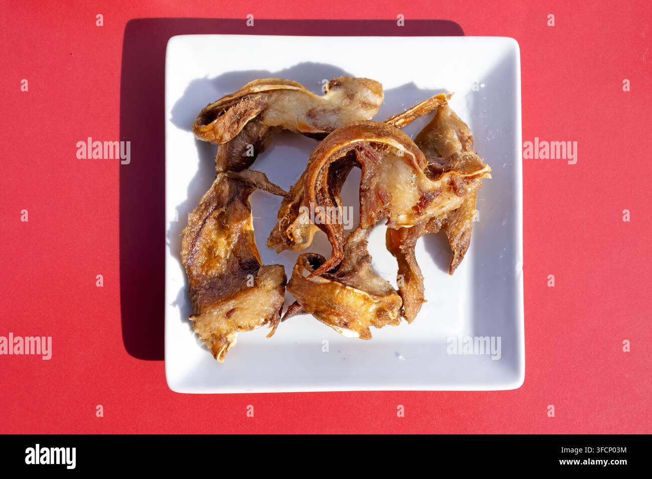 Orecchie di maiale fritte croccanti su piatto bianco con sfondo rosso Foto Stock
