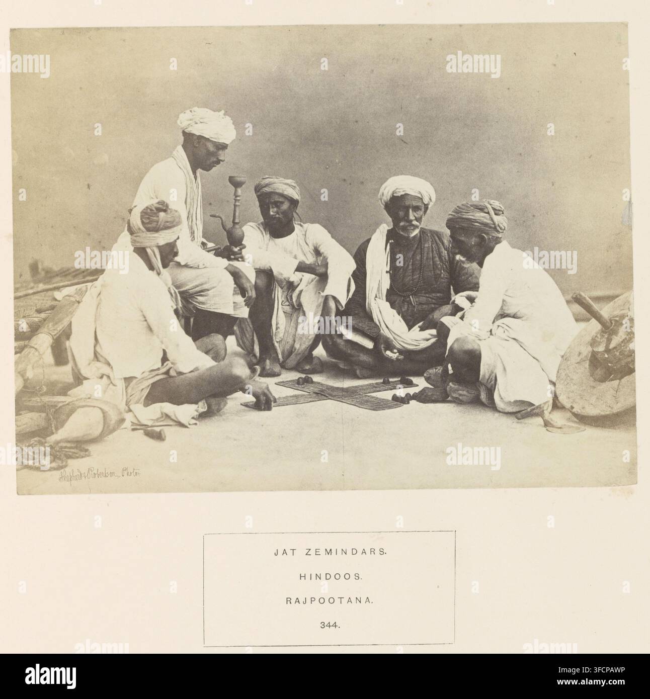 Ritratto di cinque proprietari terrieri (zamindari) della comunità Jat, Rajasthan, India, fotografia, pagina, iscrizione: 'JAT ZEMINDARS., HINDOOS., RAJPOOTANA.', numero: '344.', fotografo: Shepherd & Robertson, c. 1860 - prima del 1874, carta, stampa all'albumina, altezza 143 mm x larghezza 190 mm, pipa ad acqua, hookah, narghilè, razze umane, popoli, nazionalità, giochi da tavolo., Una fotografia seppia mostra un gruppo di uomini seduti per terra a semicerchio, vestiti con abiti ampi tradizionali e turbanti, con un uomo che tiene un alto oggetto metallico simile a un hookah mentre gli altri siedono con posture rilassate e Foto Stock