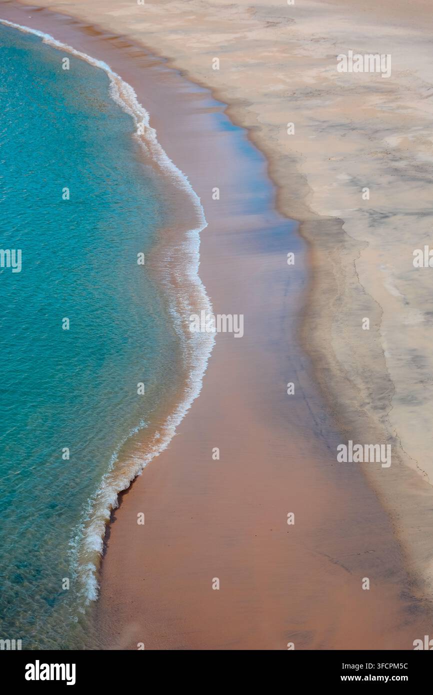 Morbide onde turchesi che incontrano una riva sabbiosa Foto Stock