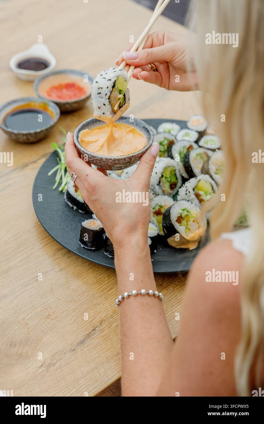 Donna che intinge un rotolo di sushi nella salsa con le bacchette Foto Stock