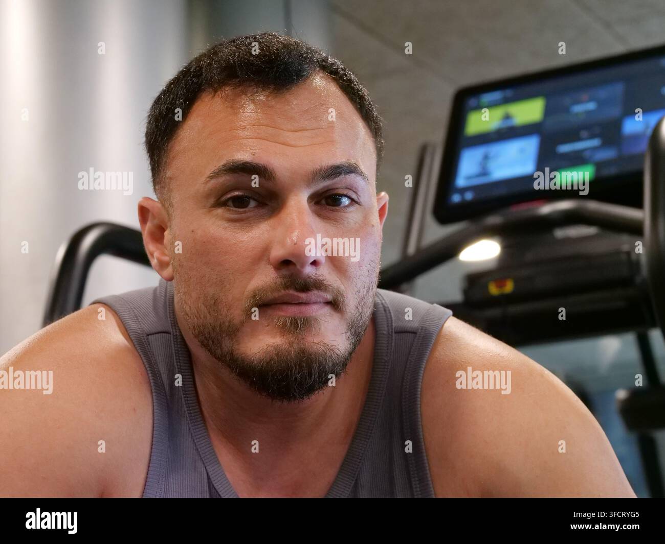 Ritratto frontale di un uomo muscoloso che fa una pausa durante la sua sessione di allenamento in palestra. Con uno sguardo determinato e sicuro di sé, incarna la disciplina, la vita atletica Foto Stock