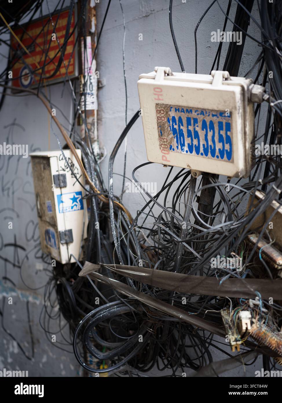 Massa caotica di cavi elettrici, fili e scatole di giunzione attaccati a un muro a Ho Chi Minh City, Vietnam, che mostrano l'infrastruttura urbana. Foto Stock