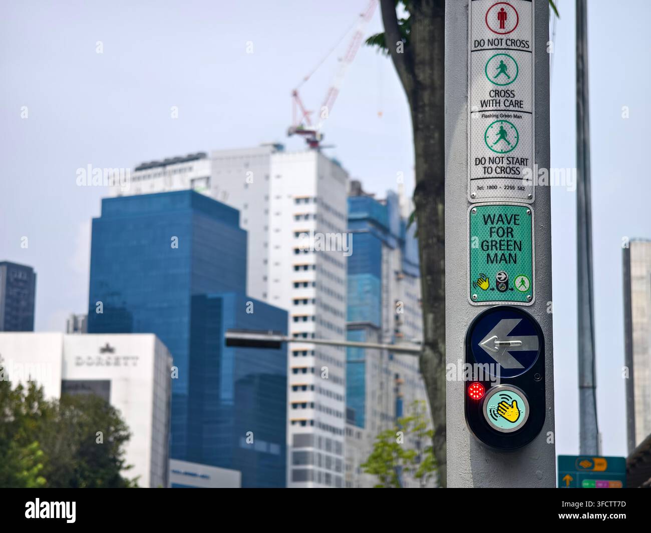 Unità a pulsante per pedoni su un palo del semaforo, dotata di un'area di sensore senza contatto con un'icona della mano luminosa e un indicatore a freccia, Singapore Foto Stock